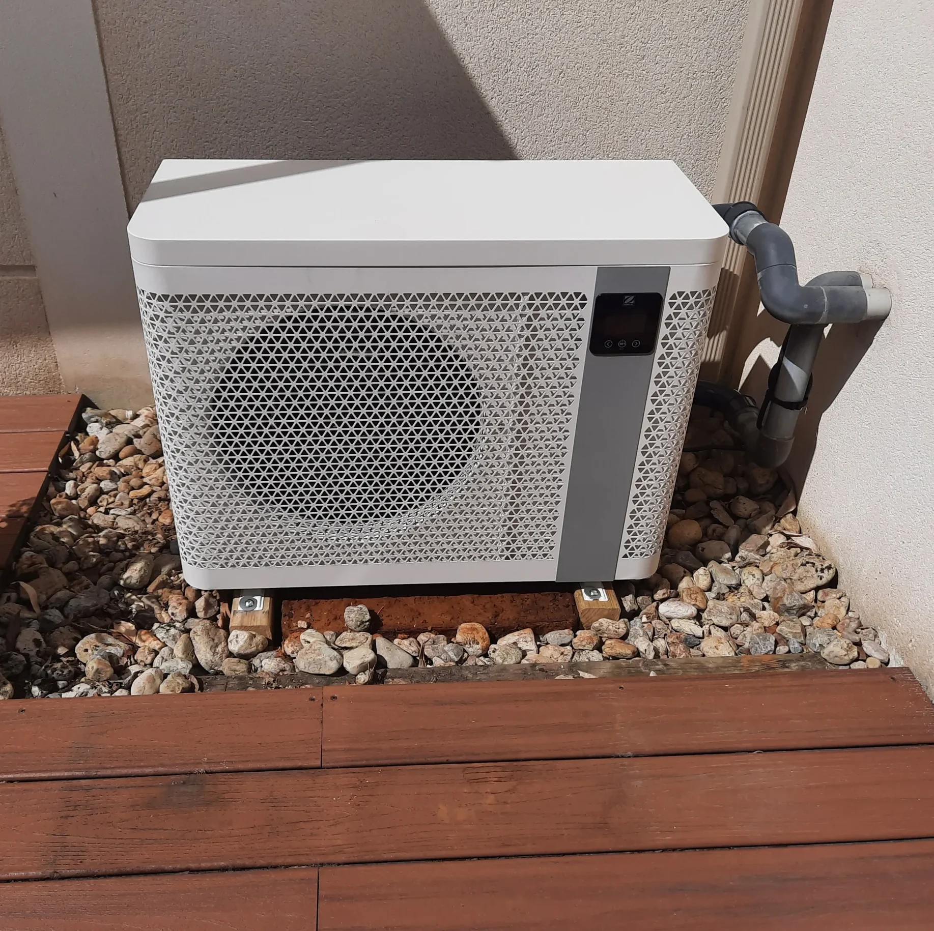 Installation d'une pompe à chaleur de piscine Zodiac près d'une terrasse en bois.